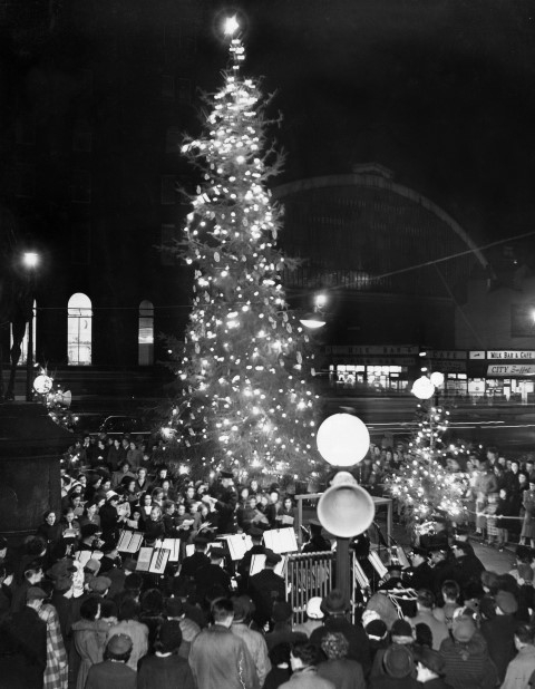 A Salvation Army band leads carol singers under magnificent tree in St George's plateau, opposite Lime Street, Liverpool. 20th December 1954 Copyright: Liverpool Echo
