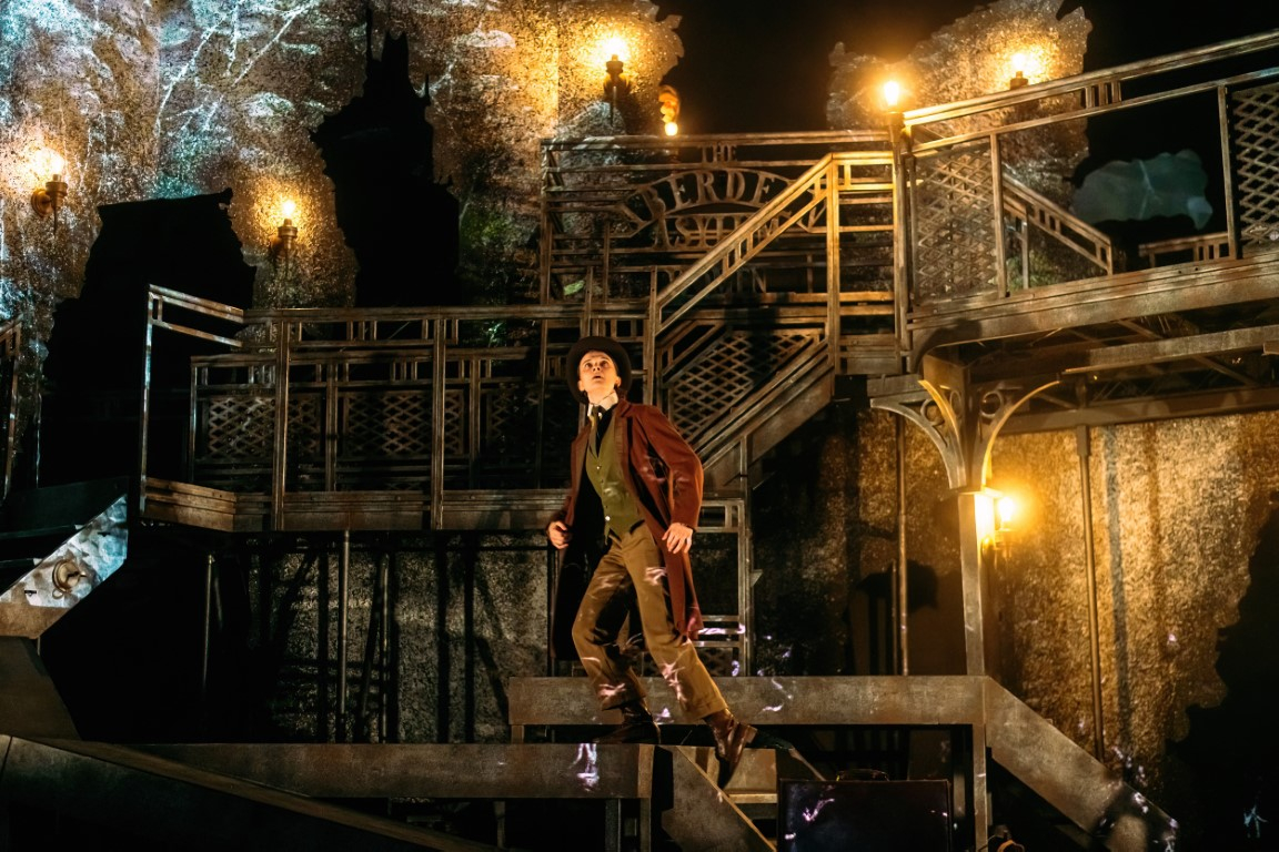 Alt text: A warm glow on stage, Jonathan looks out in fear as he runs up the stairs. 