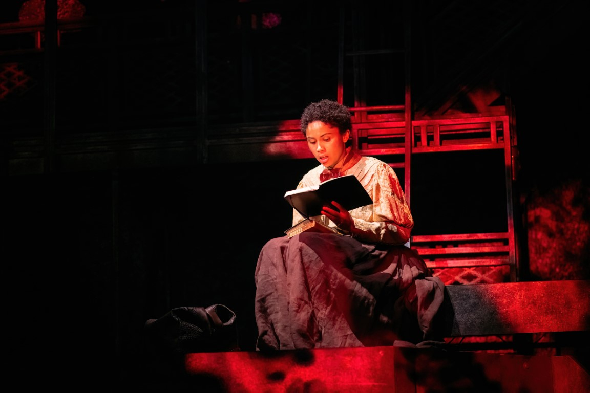 Alt text: Mina sits reading a book, another on her lap. She is surrounded by red light. 